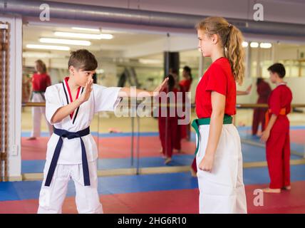 Giovani adolescenti positivi che praticano il nuovo karate si muovono a coppie in classe Foto Stock