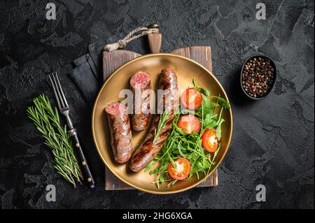 Salsicce di carne arrosto con rucola e insalata di pomodoro. Sfondo nero. Vista dall'alto Foto Stock
