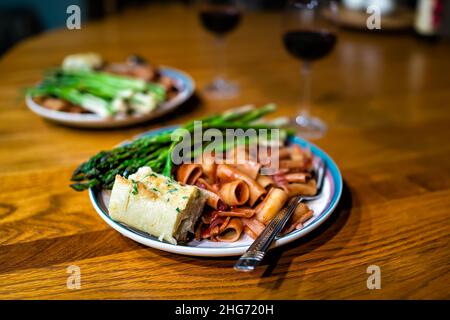Piatto da pranzo come pasto romantico con asparagi, vino rosso salsa di pomodoro rigatoni pasta su tavola di legno con pane all'aglio, forchetta e nessuno bokeh sfondo Foto Stock
