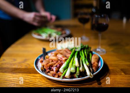 Primo piano di steli di asparagi al vapore su due piatti con vino rosso salsa di pomodoro rigatoni pasta in marinara con luce soffusa atmosfera romantica e donna Foto Stock