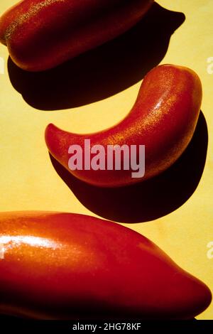 Fotografia di vita morta di pomodori rossi San Marzano su sfondo giallo con ombre dure. Foto Stock