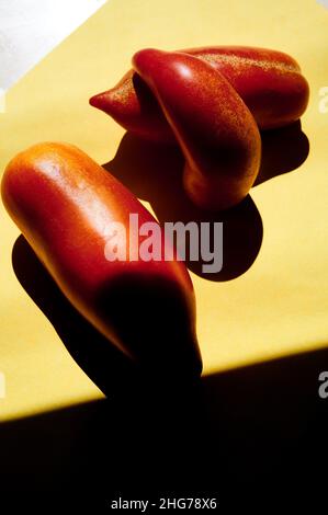 Fotografia di vita morta di pomodori rossi San Marzano su sfondo giallo con ombre dure. Foto Stock