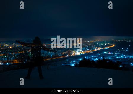 una fotografia notturna su una lunga esposizione di una silhouette trasparente di un uomo che in inverno su un'alta montagna stende le braccia ai lati Foto Stock