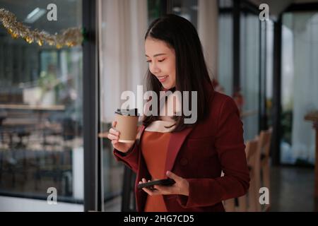 Sorridente e felice donna d'affari asiatica guardando il telefono cellulare. Concetto di finanza e contabilità Foto Stock
