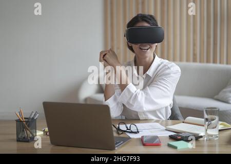 Giovane donna overjoyed gamer in occhiali di realtà virtuale giocando simulatore di gioco al lavoro Foto Stock