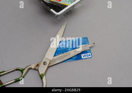 Forbici arrugginite e carte di credito in un carrello della spesa su sfondo grigio. Le forbici giacciono sulla carta di credito blu. Messa a fuoco selettiva. Kiev, Regno Unito Foto Stock