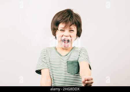 Ragazzo arrabbiato gridando e sollevando il pugno. Ragazzino aggressivo con bocca aperta guardando la fotocamera. Sindrome di ADHD Foto Stock