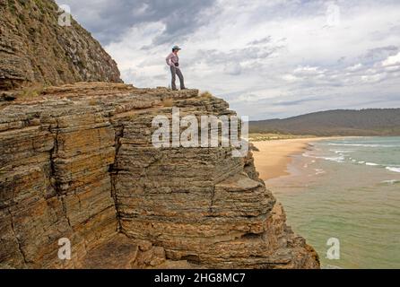 Donna in piedi in cima alle scogliere sulla Baia di Moorina, Isola Bruny Foto Stock