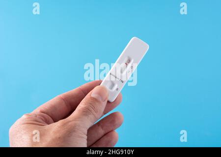 Mano che mostra il test rapido dell'antigene Covid-19 su sfondo blu Foto Stock