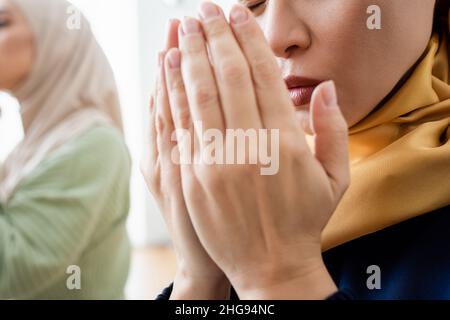 Vista ritagliata della donna asiatica che prega vicino alla figlia a casa Foto Stock