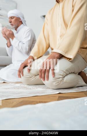 Basso angolo di vista del giovane musulmano seduto su tappeto vicino al padre che prega a casa Foto Stock