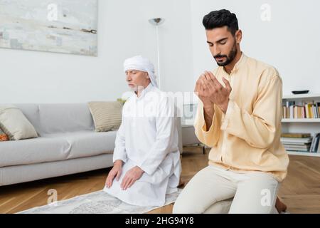Padre di età media e figlio arabo pregano a casa Foto Stock