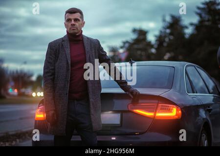Ritratto aziendale di un uomo di fronte a un'auto. Ragazzo elegante e bello nel paesaggio urbano. Foto Stock