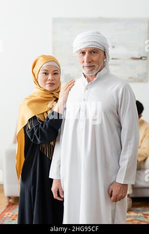 coppia interrazziale di mezza età in abiti musulmani tradizionali guardando la macchina fotografica Foto Stock