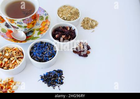Diverse varietà di tè sono sparse su un tavolo bianco. Una tazza di tè Foto Stock
