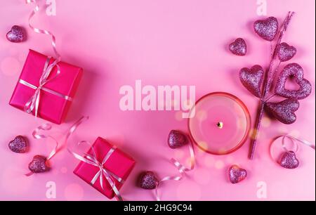 Vista dall'alto delle confezioni regalo avvolte con una candela e ornamenti a forma di cuore su sfondo rosa Foto Stock