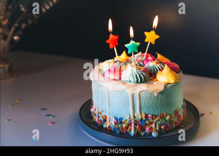 Torta di compleanno colorata con spolverini e candele a forma di stella brucianti su sfondo scuro parete. Festa di compleanno, festa. Messa a fuoco selettiva, Foto Stock