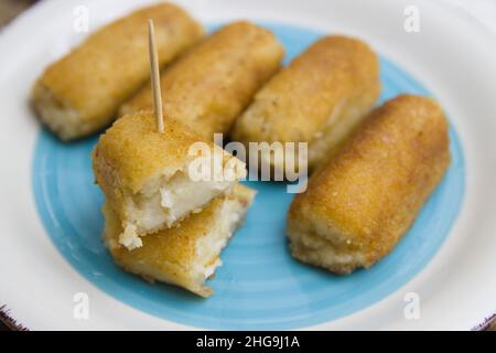 Piatto con crocchette preparate industrialmente su un piatto con fondo blu, una delle crocchette è attraversata con uno stuzzicadenti come una Tapa Foto Stock