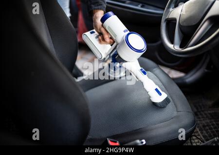 Pulizia dell'interno del sedile dell'auto con aspirapolvere portatile Foto Stock