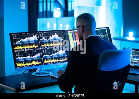 L'uomo commerciante di riserva usando i monitor multipli del calcolatore Foto Stock