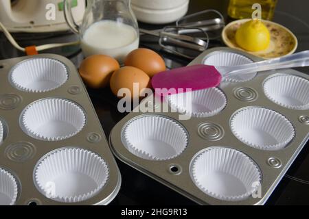 Preparazione di alcuni muffin fatti in casa, alcuni degli ingredienti necessari (farina, latte, uova, limone, olio), gli stampi per muffin, il mixer e una pala Foto Stock