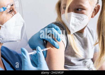 Bambina in maschera in ufficio medico ottenere vaccinato. Siringa con vaccino per il co-virus-19 coronavirus, influenza, malattie infettive pericolose. Injetti Foto Stock