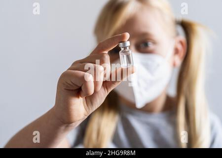 La ragazza bionda con maschera facciale mostra un flacone di vaccino per il vaccino Covid-19 in un centro di vaccinazione. Foto Stock