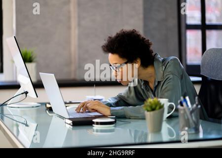 Donna africana cattiva postura che lavora digitando alla scrivania Foto Stock