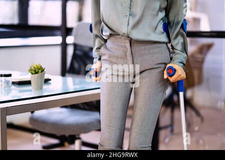 Donna d'affari handicappata che cammina con le stampelle sul posto di lavoro Foto Stock