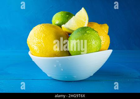 Limoni e lime interi e tagliati a fette in una macro di primo piano bianca su sfondo blu. Foto Stock