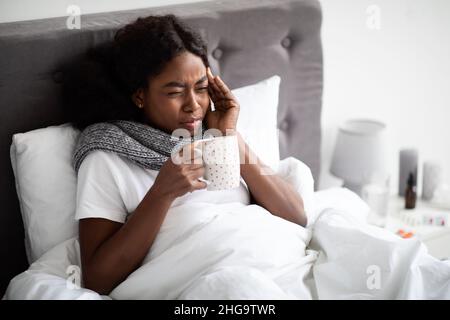 Donna nera che si stendeva a letto con una tazza di bevanda calda Foto Stock