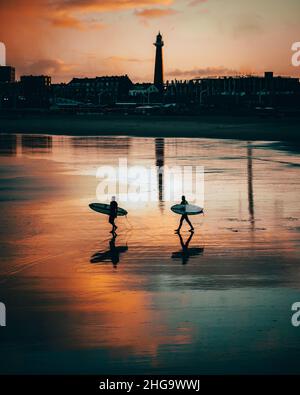 Due surfisti che camminano verso il mare nella gloria del mattino Foto Stock