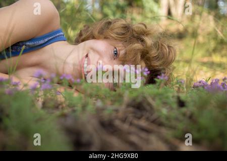 faccia della ragazza adolescente che giace sull'erba con i piccoli fiori, godendo la natura all'aperto. La giovane donna carina sta riposando nel parco. Primavera, estate, sole. dre Foto Stock