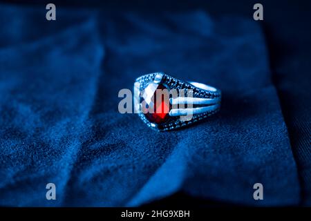 Un'immagine ravvicinata di un anello d'argento con pietra rossa su sfondo blu Foto Stock