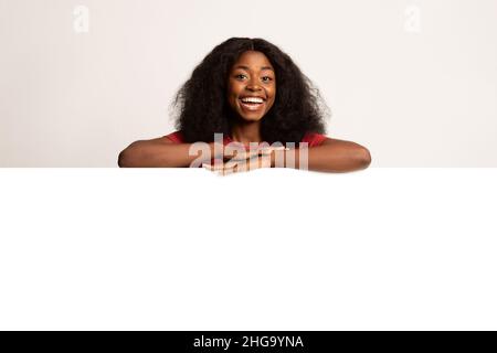 Cheerful Black Female Leaning at Big White Blank Advertisement Board Foto Stock