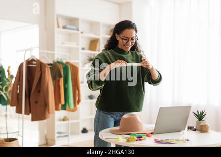 Designer femmina che prende foto di cappello su smartphone in showroom Foto Stock