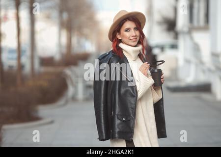 Ritratto di moda urbana di donna millenaria elegante in abiti moderni a piedi sulla strada della città con caffè Foto Stock