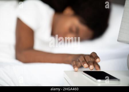 Donna nera che si stenderà a letto, spegnendo l'allarme sul cellulare Foto Stock