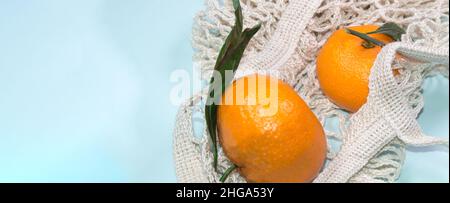 Sfondo blu con tangerini in una borsa a corda. Stile di vita sano, vista dall'alto, zero sprechi. Foto Stock