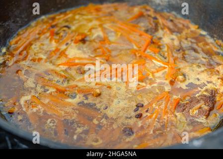 La carne con carota viene cotta nel calderone al fuoco. Cottura passo dopo passo del Pilaf. Foto Stock
