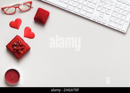 Desktop per San Valentino. Tastiera rosso cuore dono occhiali candela su tavola grigia. Vista dall'alto dello spazio di copia a disposizione piatta Foto Stock