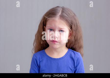 Bambino triste e infelice con lacrime di sofferenza, dolore o dolore su sfondo grigio guardando la fotocamera ritratto di caucasica bambina di 5 anni in Foto Stock
