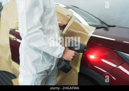 Il pittore d'auto illumina una luce speciale sulla carrozzeria del veicolo per scegliere la giusta tonalità Foto Stock
