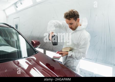 L'uomo pittore determina la tonalità corretta del colore della carrozzeria di un veicolo utilizzando una lampada speciale. Autorimessa in garage Foto Stock