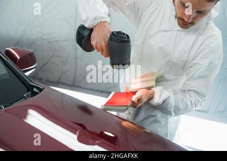 L'uomo pittore determina la tonalità corretta del colore della carrozzeria di un veicolo utilizzando una lampada speciale. Autorimessa in garage Foto Stock