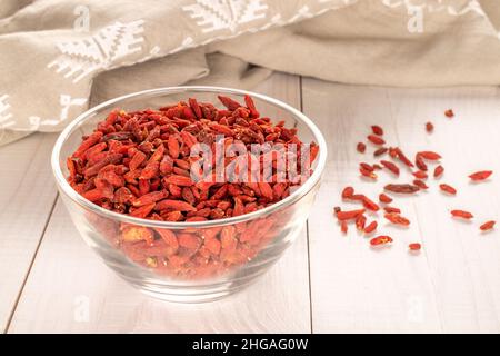 Bacche di goji essiccate in un piatto di vetro su un tavolo di legno, macro. Foto Stock