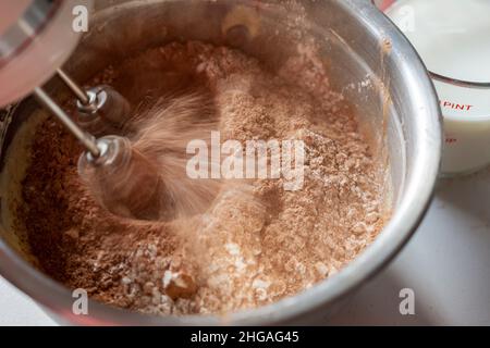 Preparazione di una torta al cioccolato: Aggiunta di ingredienti secchi. Fruste del mixer in movimento con sfocatura del movimento. Foto Stock