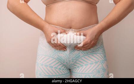 Donna grassa usando le sue mani per spremere fuori grasso in eccesso che è isolato su uno sfondo beige. Foto Stock