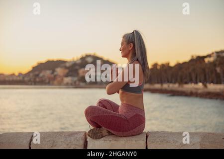 Donna sportiva meditante in posizione lotus al mare Foto Stock