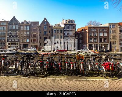 Street ad Amsterdam, le biciclette sono allineate lungo le ringhiere accanto a un canale. Edifici in tipico stile Olandese sullo sfondo. Foto Stock